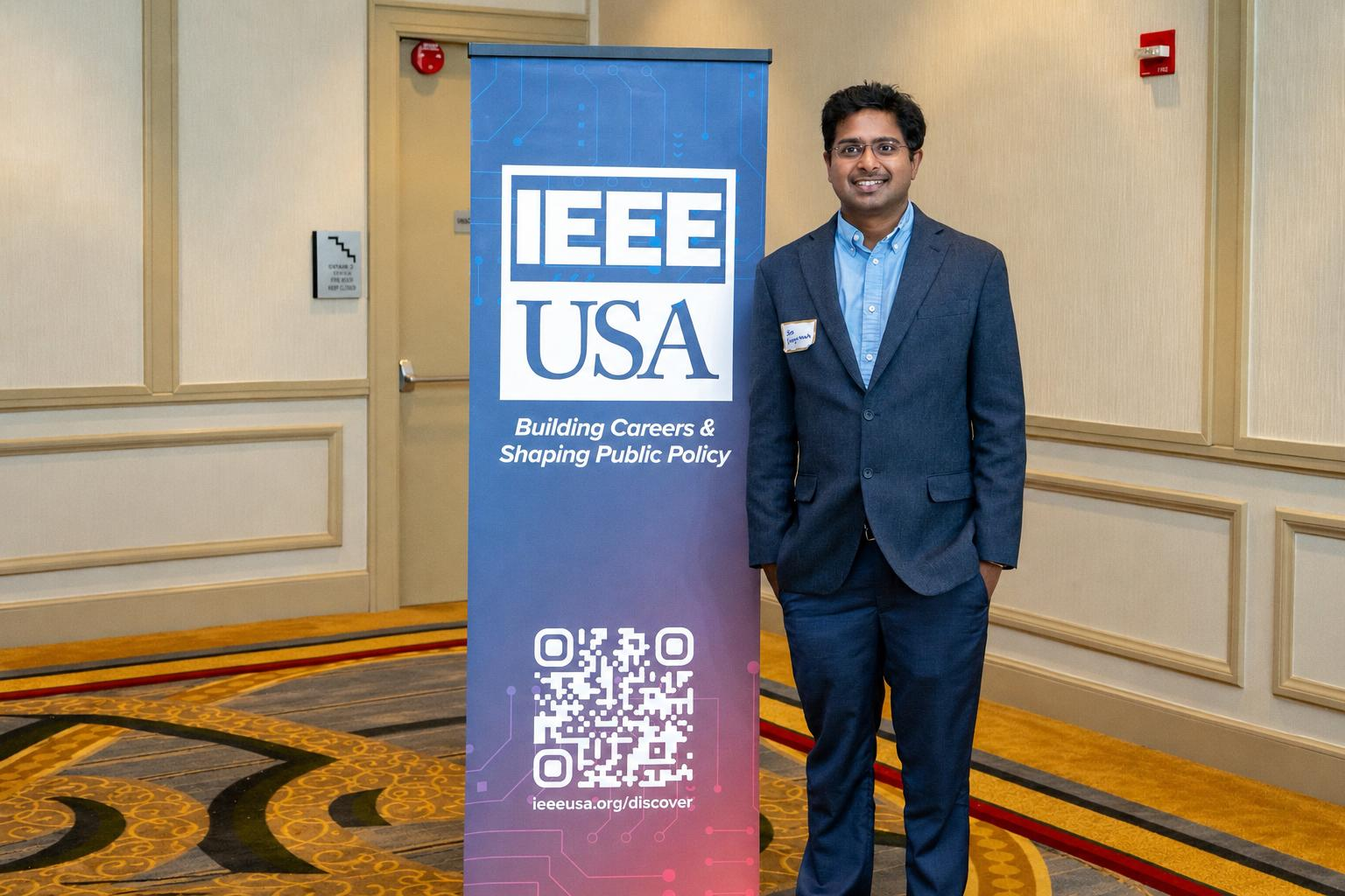 Siva Bayyavarapu standing next to an IEEE-USA banner at a professional event